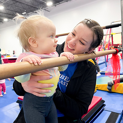 Parent helps toddler on bar practice gripping during gymnastics class